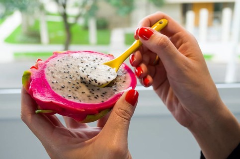 Woman hand eating pitaya with colored spoon