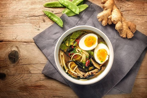 Miso soup with noodles, nori seaweed, snow peas, ginger and an egg in a bowl on a rustic wooden