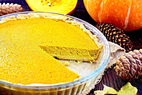 Pumpkin pie in a glass pan on sackcloth, pumpkins, pine cones and maple leaf on the background of