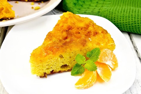 Piece of tart with mandarin, mint, mandarin slices in a white plate, towel on a background of