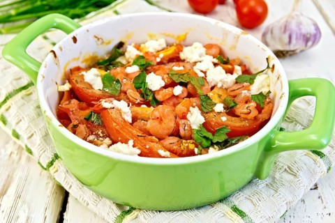 Shrimp and tomatoes baked with feta cheese in a roasting pan on a towel, parsley and garlic on a