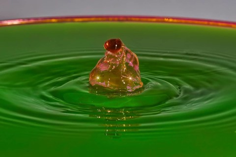 A reddish-brown drop hits green liquid and forms water rings, water droplets, collision, high-speed
