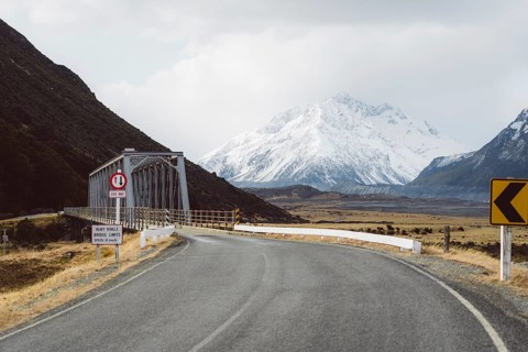 Road leading to a bridge with snow-capped mountains and cloudy sky in the background, Hooker Valley