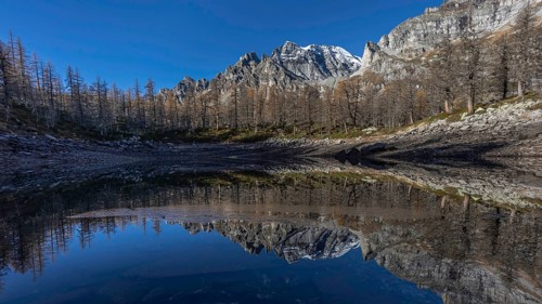 A tranquil mountain lake reflects the surrounding snow-capped mountains and clear blue sky, Lago