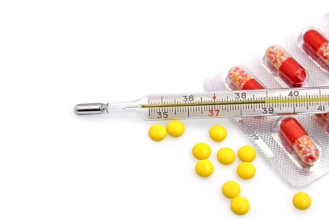 Thermometer with the yellow pills in bulk and red-white capsules in a package on a white