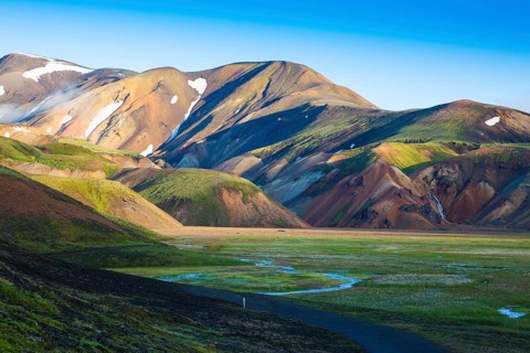 Snow lies in the hollows of colorful rhyolite mountains. Green Valley is flooded with melt water.