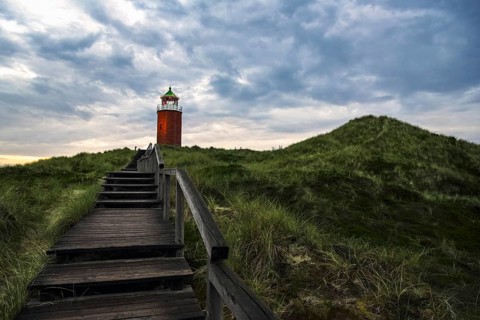 Evening landscape with wooden stairs over marram grass hill, toward red lighthouse, on Sylt island,