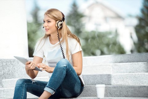 Happy young woman with vintage headphones and a cup of coffee to go, surfing the internet on a