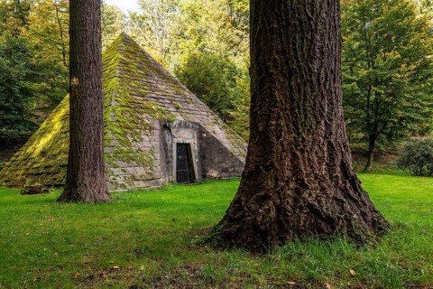 Pyramid-shaped, moss-covered mausoleum, surrounded by tall trees, mystical atmosphere,