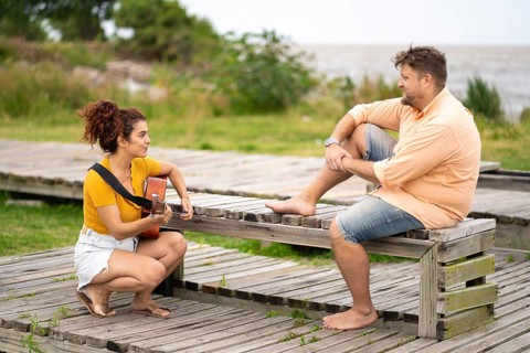 Women squatting playing guitar for her boyfriend in a park near the sea