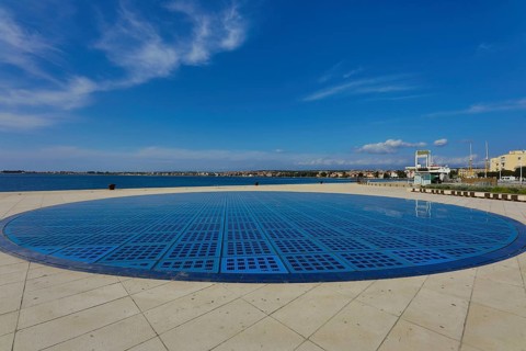 Modern circular solar installation by the sea with clear sky and calm surroundings, artwork