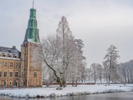 Castle in winter, surrounded by snow-covered trees, with a frozen lake in the foreground, Raesfeld,