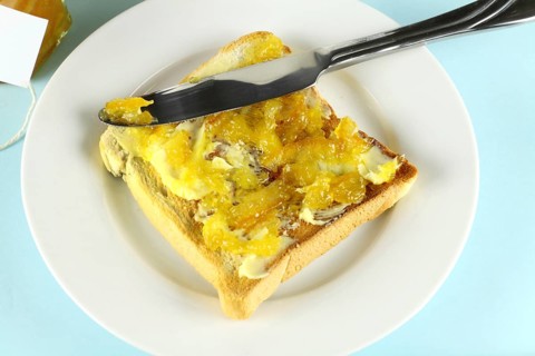 Orange marmalade spread on a slice of toast with butter
