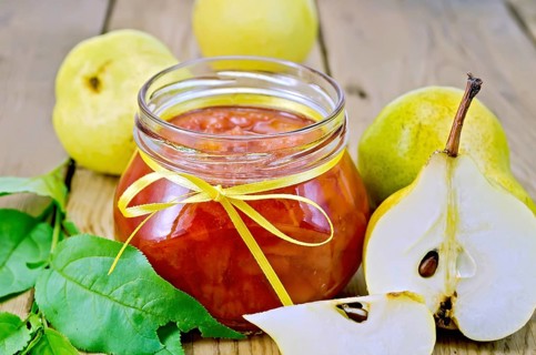 Pear jam in a glass jar, fresh pears, twigs with leaves on a wooden board