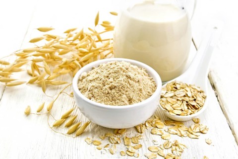 Flour oat in bowl, milk in a jug, oatmeal in spoon, oaten stalks on the background of light wooden