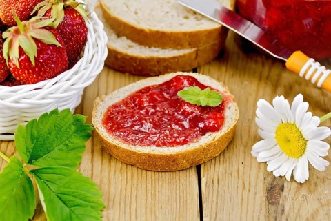 Bread with strawberry jam, a jar of jam, knife, strawberries in a wicker basket, chamomile on a