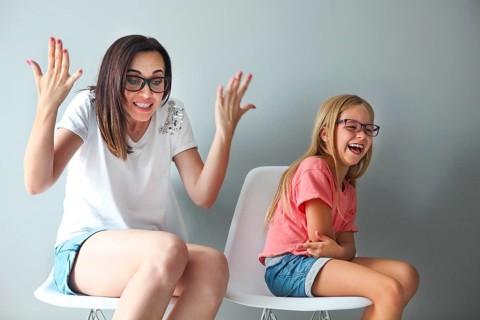 Happy mother and her little daughter sitting on the chairs by the grey wall. Portrait of mother and