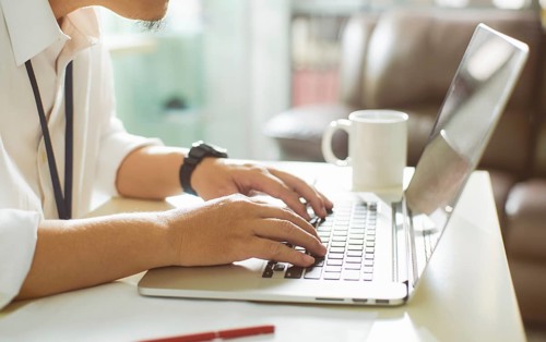 Businessman using laptop with tablet and pen on white table in office with a cup of coffee, side