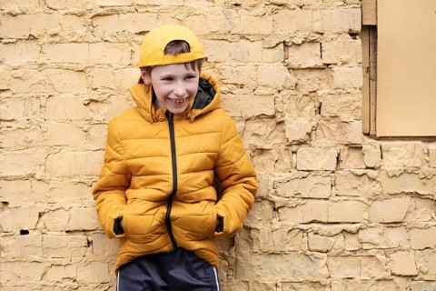 A child on the street A cheerful boy in yellow clothes and a baseball cap stands against a brick