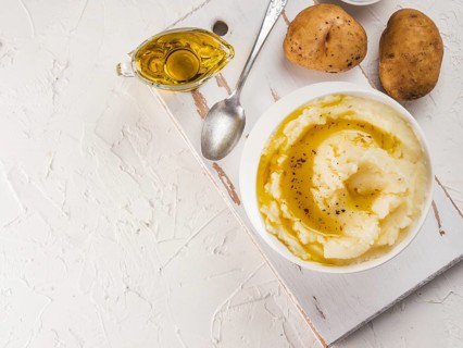 Mashed potatoes in white bowl on white cutting board, pepper and olive oil on white concrete