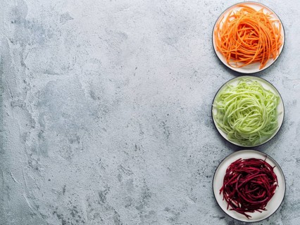 Vegetable noodles - zucchini, carrot, and beetroot noodles on plate over gray cement background.