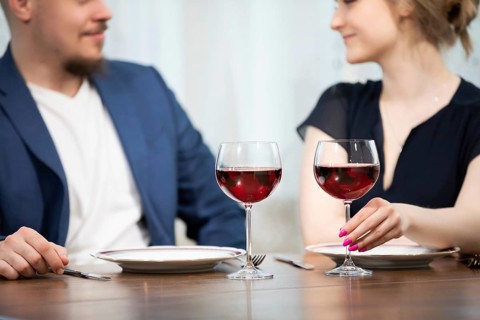 A man and a woman sit at a table. Both are elegantly dressed. On the table are two plates and two