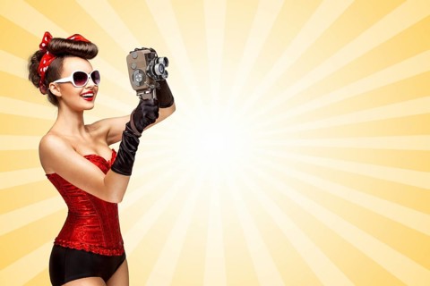 Retro photo of a glamorous pin up girl with an old vintage cinema 8mm camera shooting a film on
