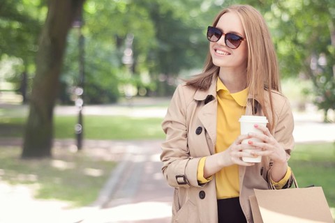 Young fashionable woman taking a coffee break after shopping and walking with a coffee to go in her