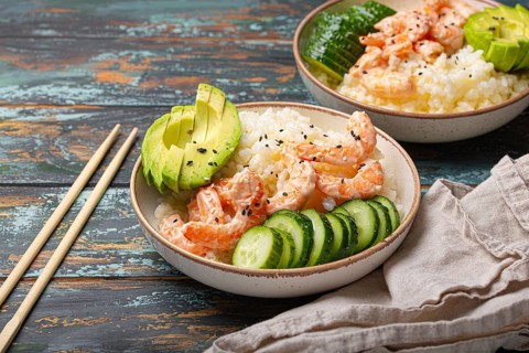White ceramic bowl with rice, shrimps, avocado, vegetables and sesame seeds and chopsticks on