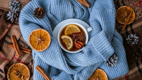 Blue sweater and cup of hot tea with lemon cinnamon sticks and anise star. Dry slices of citrus