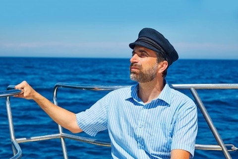 Beard sailor man sailing sea ocean in a boat with captain cap looking horizon