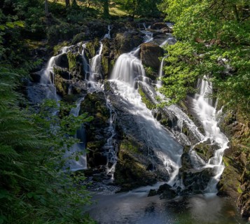 A view of the Swallow Falls waterfall in Anglesey in northern Wales surrounded by lush green summer