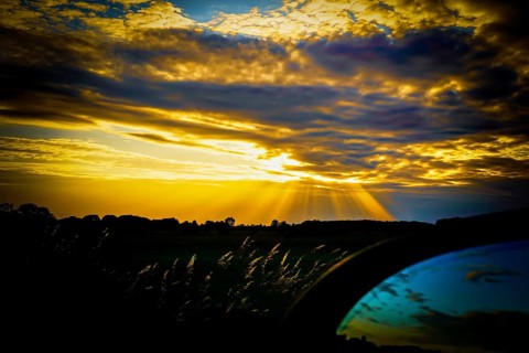 A dramatic sunset with yellow and blue tones, rays of light through clouds and a dark silhouette in