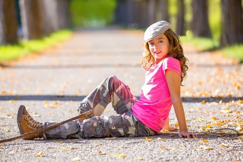 Autumn kid girl with camouflage pants sitting resting in fall trees track with hiker branch stick