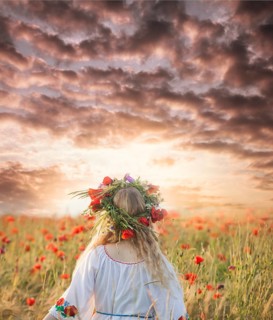 Pretty blonde girl in a dress with a pattern poppy and with a wreath on his head enjoying in a