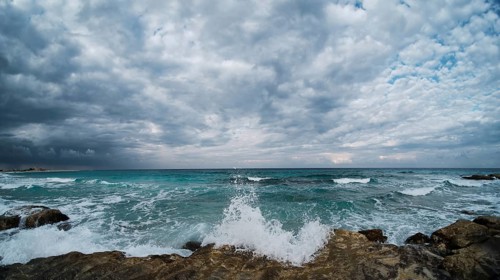 Waves of rushing sea are crashing over rocky coastline. Sea waves break upon rocks. Ultra-wide