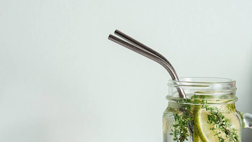 Cold drink in mason jar with metal straw on white background. Lemonade or detox water with lime and