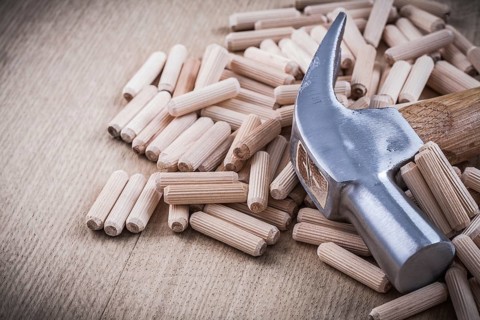 Dowel pins and claw hammer on wooden board construction concept