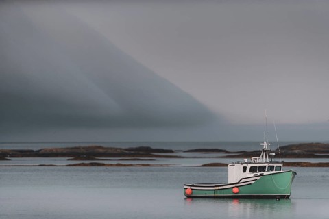 A commercial fishing boat sits tied to its mooring with dramatic clouds above, behind it are shoals