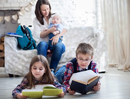 Son and daughter with their mother and little brother siting on the sofa. Children readind books in