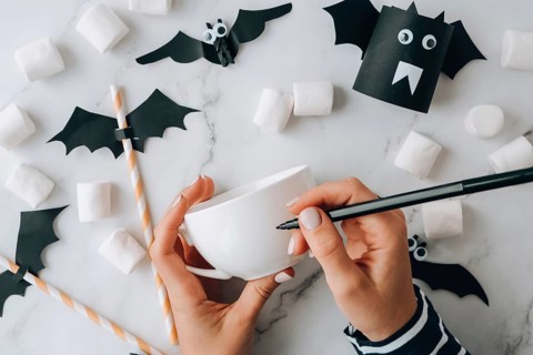Female hands paint on white cup scary jacks face DIY for kids Halloween home activities Holiday art