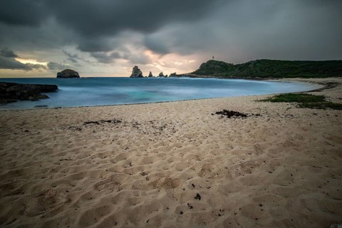 A secluded bay with a sandy beach in the morning. At the end of the beach a pointed rock formation