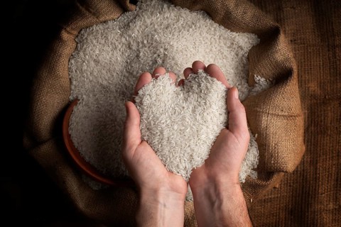 Human hands in shape of heart holding handful of rice over burlap sack