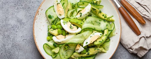 Healthy green avocado salad bowl with boiled eggs, sliced cucumbers, edamame beans, olive oil and