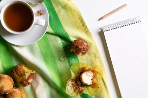 Above view of a breakfast table with a cup of linden tea, muffins on a green and yellow towel and