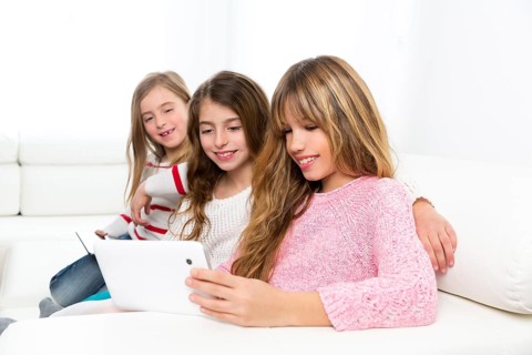Three kid sister friends girls group playing together with tablet pc on white sofa