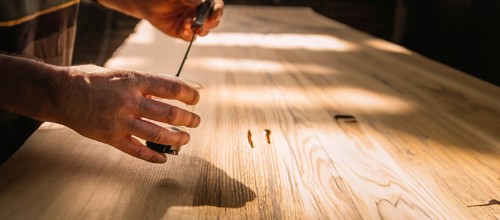 Close-up of hands working on a wooden tabletop, with sunlight creating a serene working environment