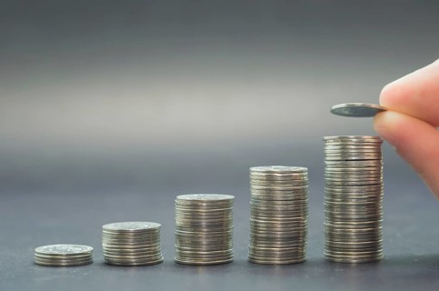 Great concept of savings, economy. Hand adding coin into pile of coins