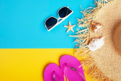 Straw hat sunglesses flip flops and shells on yellow and blue background vacation travel planning