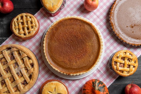 Above view of a table with a pink towel, full of various homemade pies, pumpkin pies, apple pies,